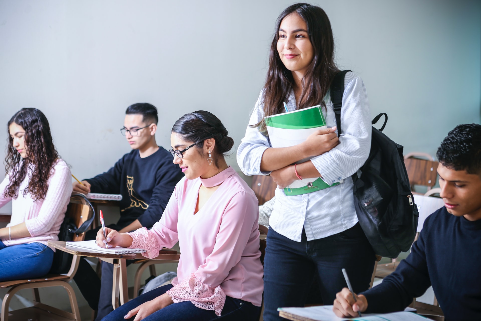 Image of five students studying in a classroom with one walking to her seat