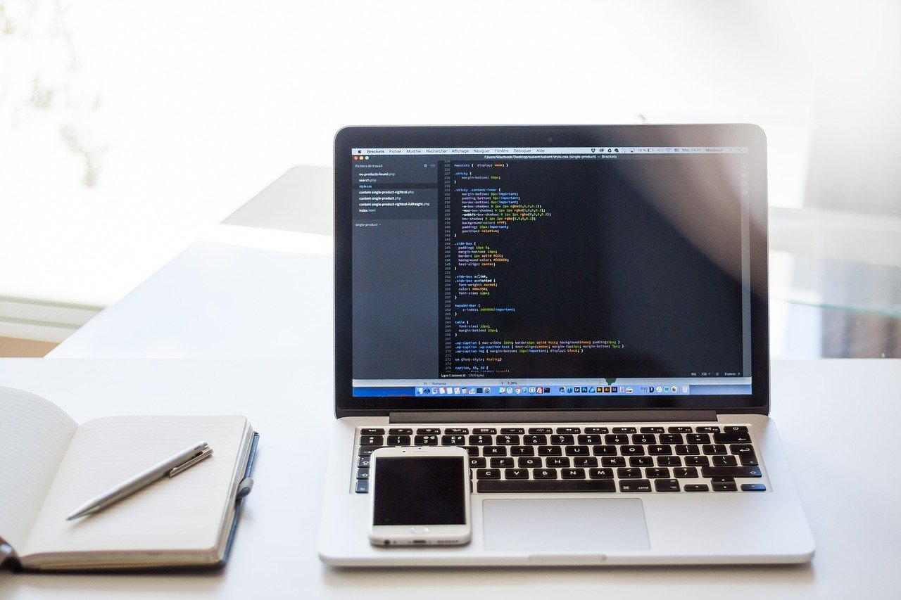 Mac laptop, iPhone, and notebook on a white desk.